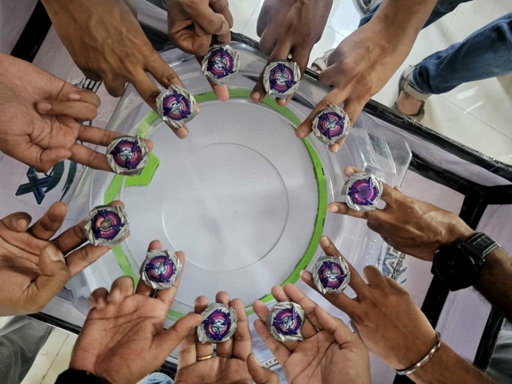 Players holding Beyblades over a battle stadium in a circle, seen from above